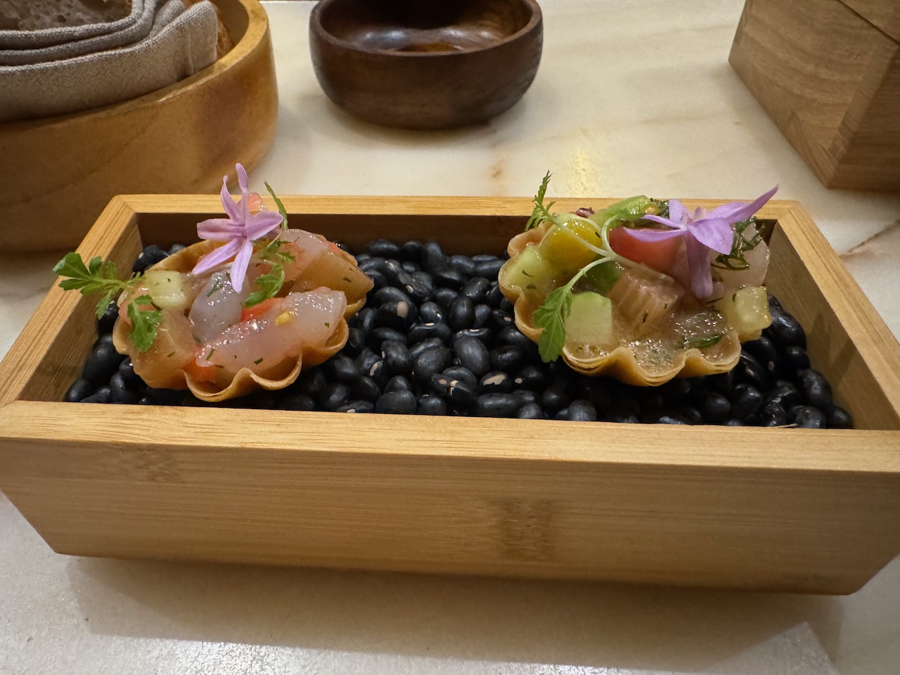 Two servings of seafood on black pebbles in a box.